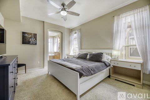 A bedroom with a large bed, a ceiling fan, and a painting on the wall.