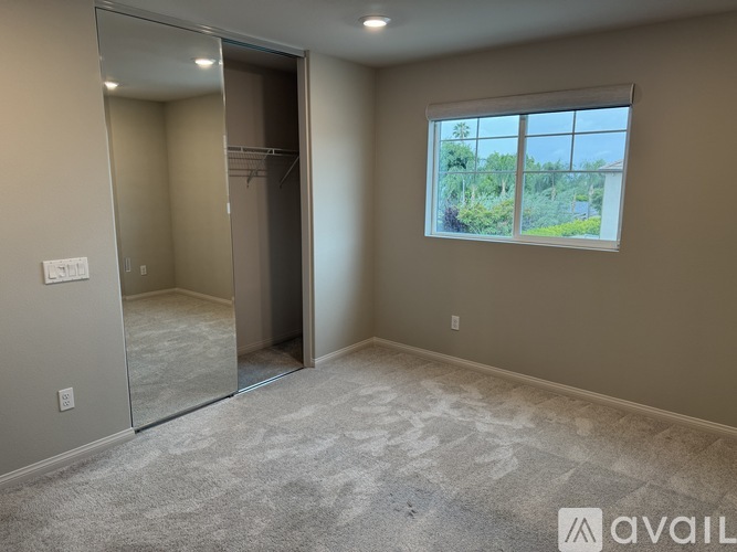 A spacious room with a carpeted floor, a large window, and a glass door leading to another room.