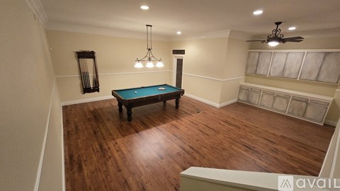 A pool table in a room with wood flooring and a ceiling fan.