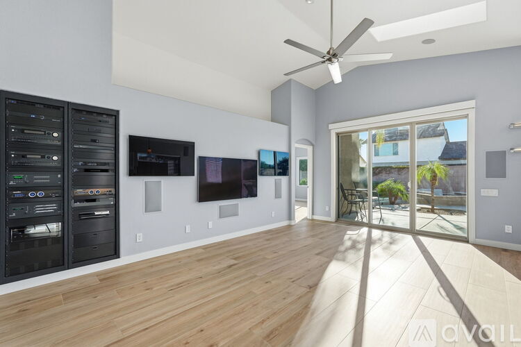 A spacious room with a ceiling fan, wooden flooring, and a view of the outdoors through a sliding glass door.