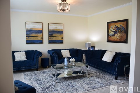 A living room with blue couches and a painting on the wall.