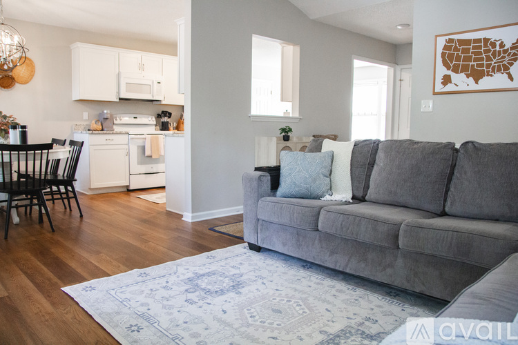 A living room with a grey couch and a kitchen area in the background.