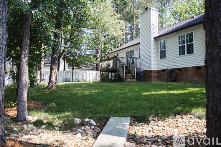 A white house with a brick chimney is surrounded by trees.
