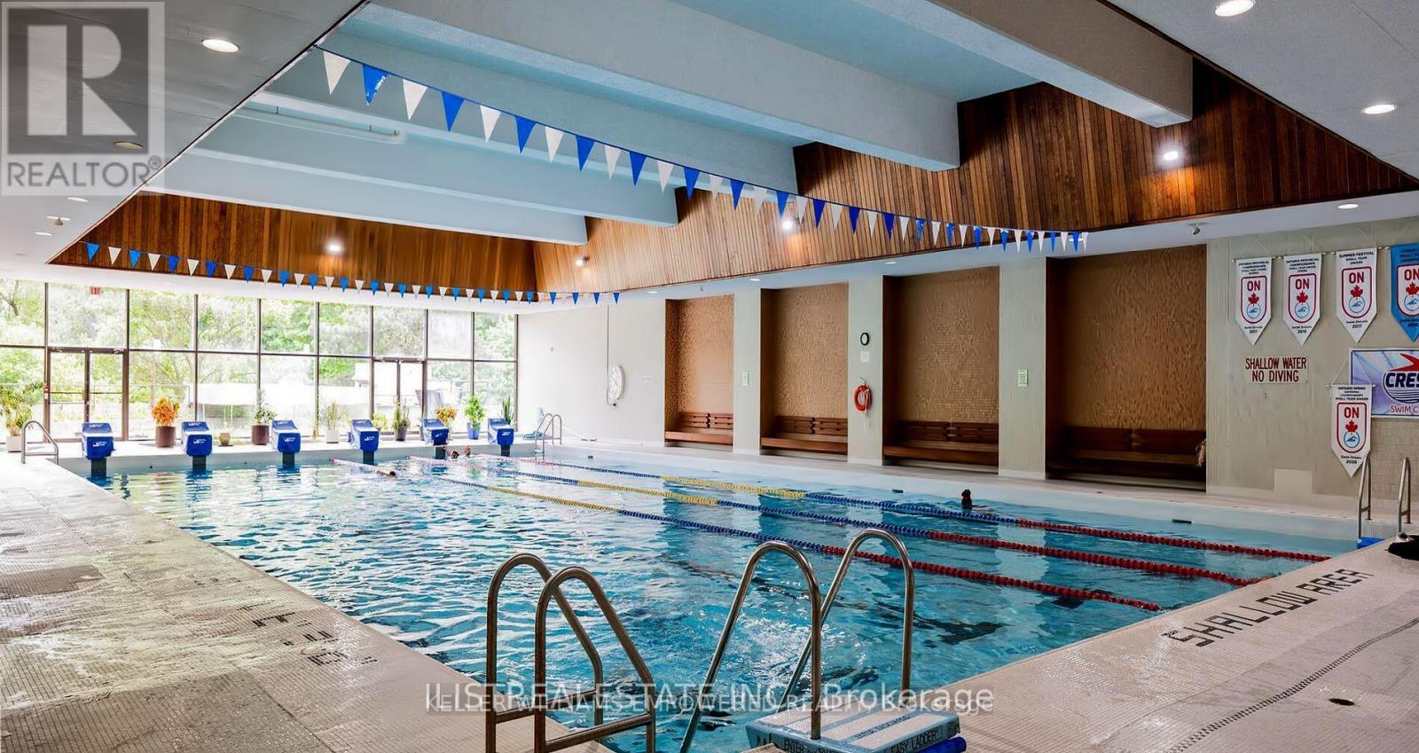 A large indoor swimming pool with a diving board and flags hanging from the ceiling.