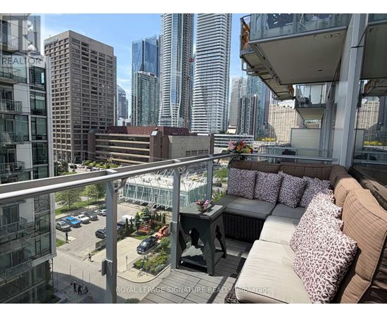 A balcony with a couch and pillows overlooks a cityscape.