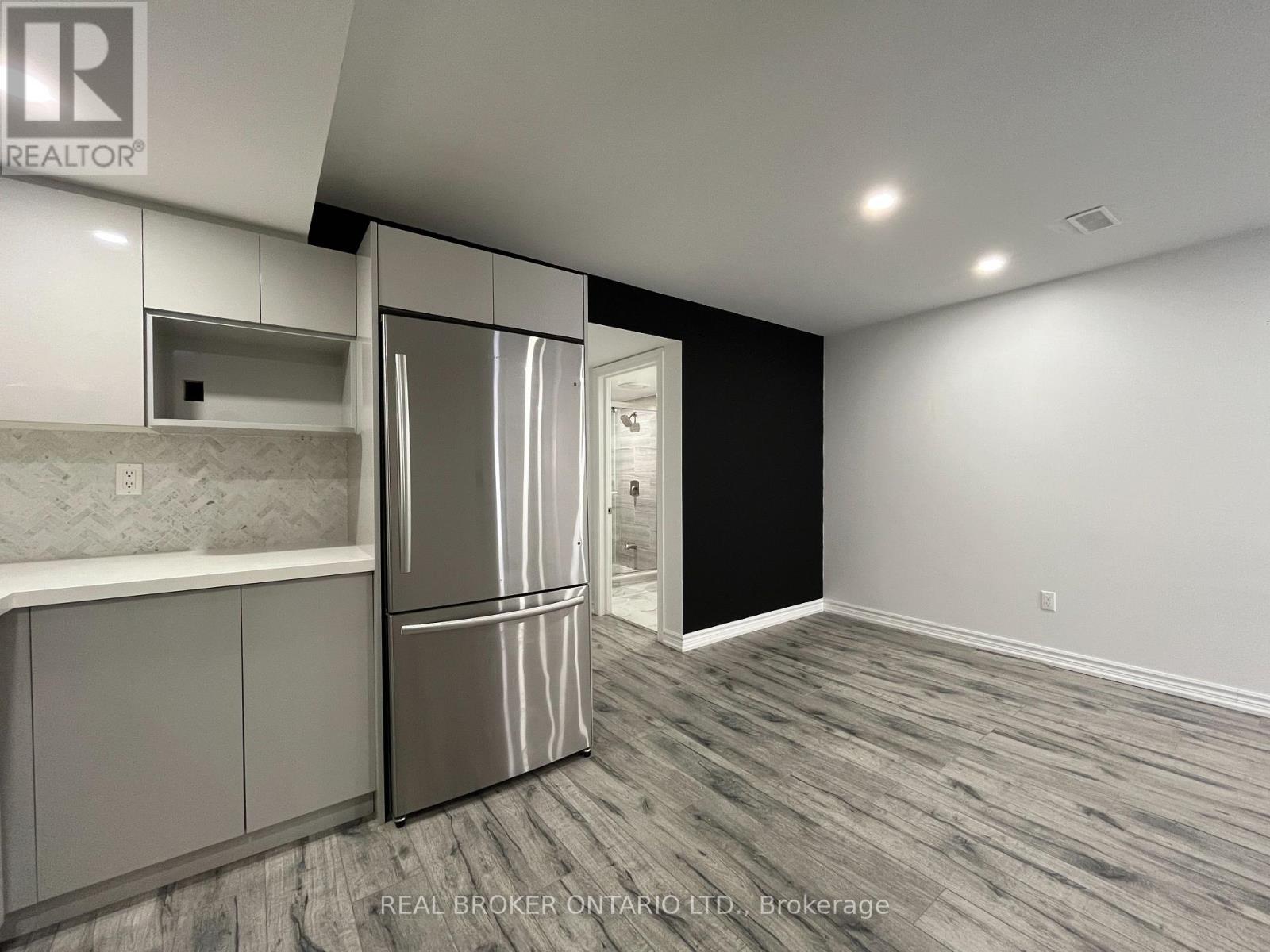 A kitchen with a refrigerator and cabinets in a room with wood flooring.