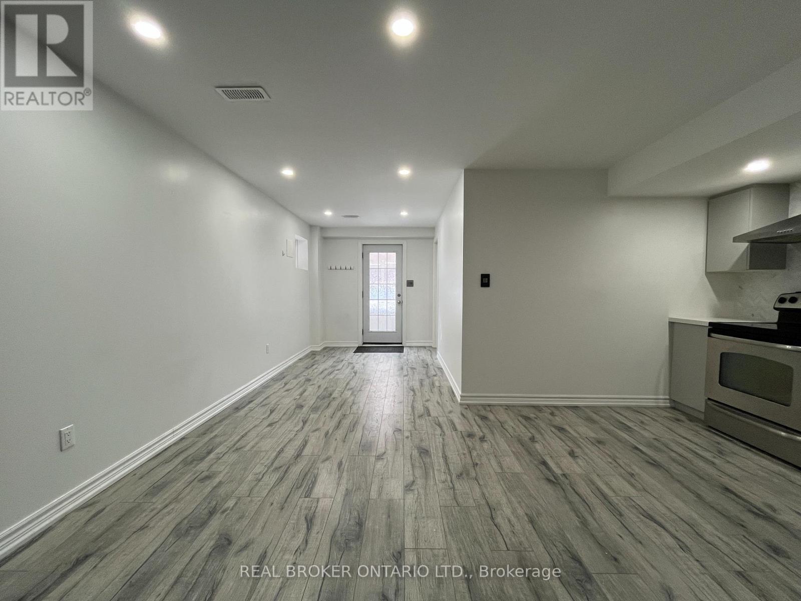 A spacious room with wood flooring and a kitchenette in the background.