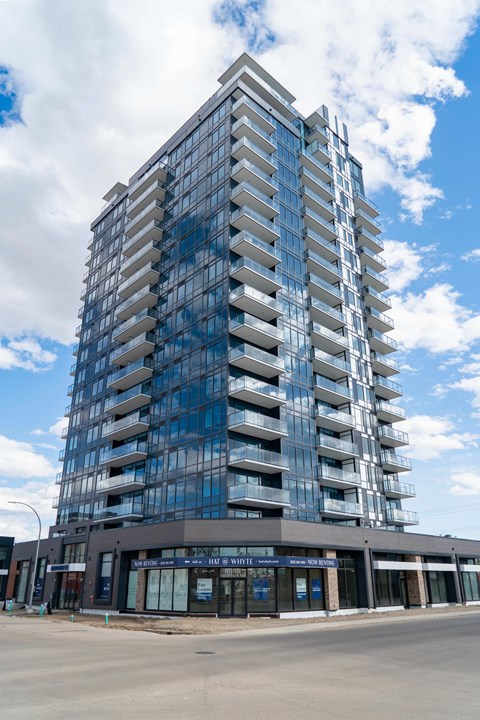A tall building with many windows and balconies is under a blue sky with clouds.