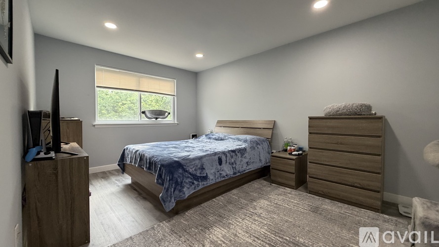 A bedroom with a bed, dresser, and a window with blinds.