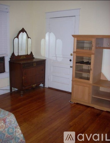A room with a wooden floor, a white door, a wooden cabinet with glass doors, and a wooden dresser with a mirror on top.