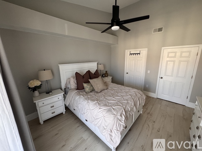 A bedroom with a large bed, a ceiling fan, and a nightstand with a lamp.