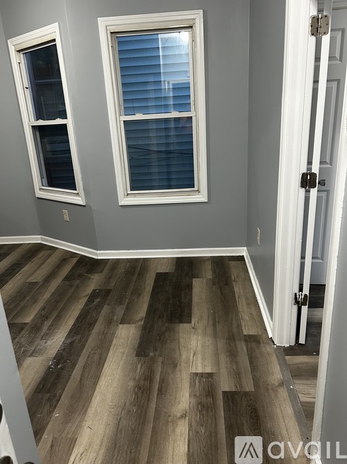 A room with a white door and two windows with white frames and wooden flooring.