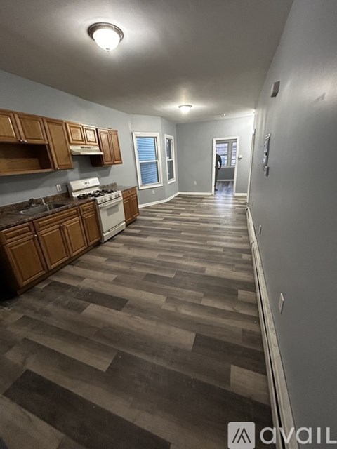 A long hallway with wood flooring and a kitchen area with wooden cabinets and a stove top oven.