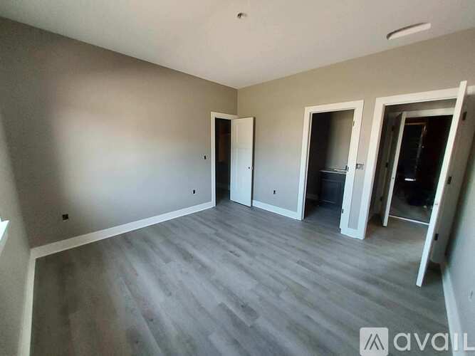 A room with grey walls and wooden flooring, with three doors and a window.
