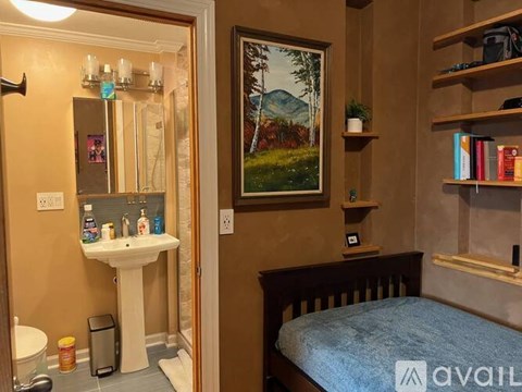 A bathroom with a white pedestal sink and a bedroom with a bed and a painting on the wall.