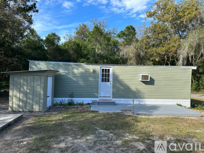 A small house with a white door and a window is surrounded by trees.