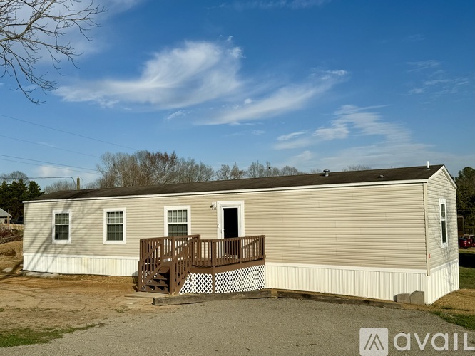 A mobile home with a deck and a small tree in the background.