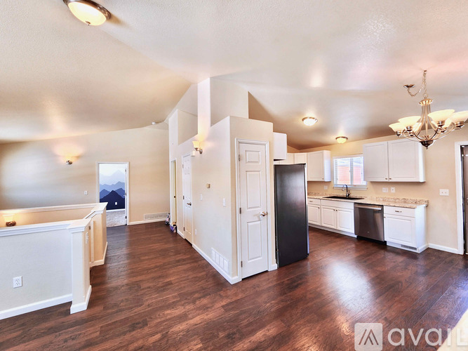 A large open living room with wood floors and a kitchen area with white cabinets and appliances.