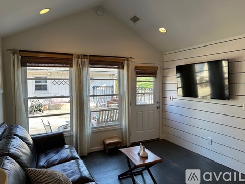 A living room with a black leather couch and a flat screen TV mounted on the wall.