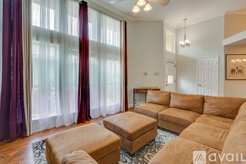 A living room with a tan couch and ottoman, a coffee table, and a large window with red curtains.