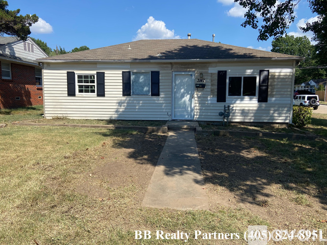 A small white house with a brown roof and a sign that says BB Realty Partners.
