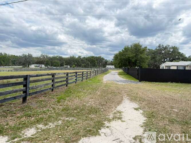 A dirt path leads through a grassy area with a wooden fence on the left and a metal fence on the right.