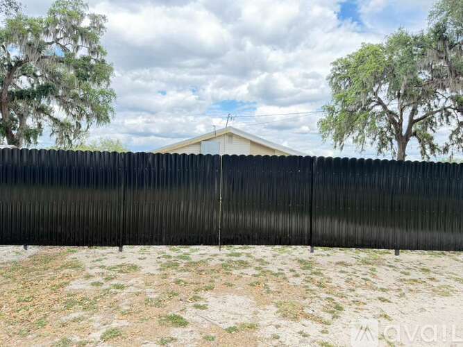 A black fence in front of a house with trees in the background.