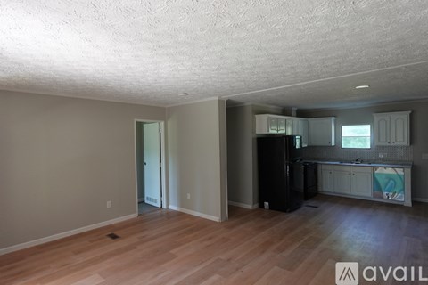 A room with wooden floors and a kitchen area with a fridge and cabinets.