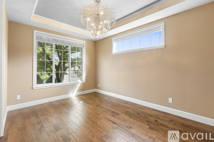 A room with a chandelier, two windows, and wooden flooring.