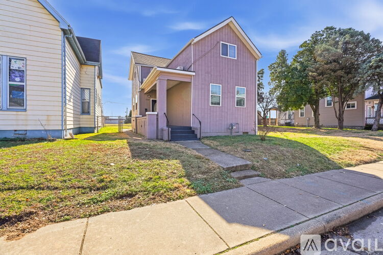 A house with a pink exterior is in the foreground with a grassy front yard.