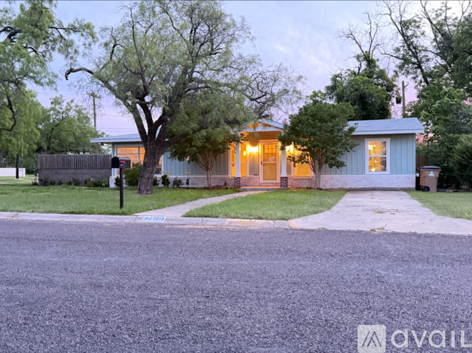 A house with a lit up front porch and a tree in front of it.