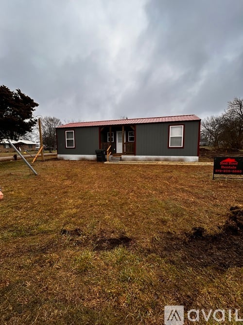 A small house with a red roof is situated in a grassy field.