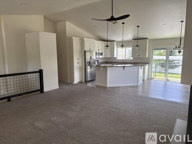 A spacious kitchen and living room with a fan and a black railing.