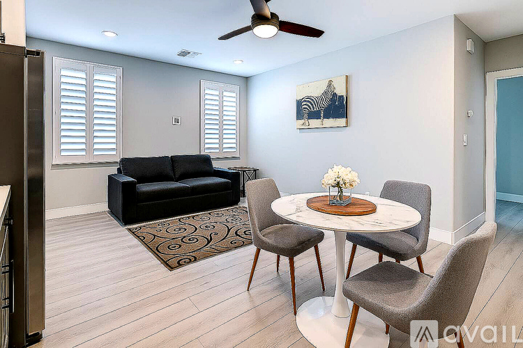 A living room with a black couch, a round table with chairs, and a ceiling fan.