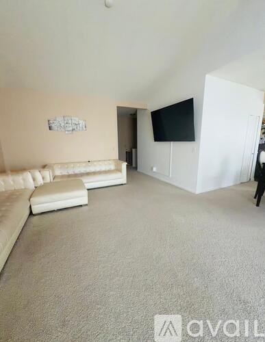 A living room with a white couch and a flat screen TV mounted on the wall.