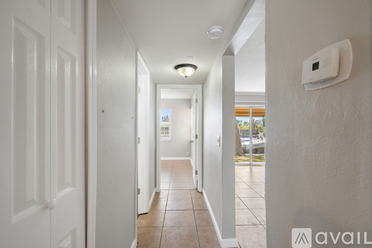 A hallway with a white door on the left and a white wall on the right with a thermostat on it.