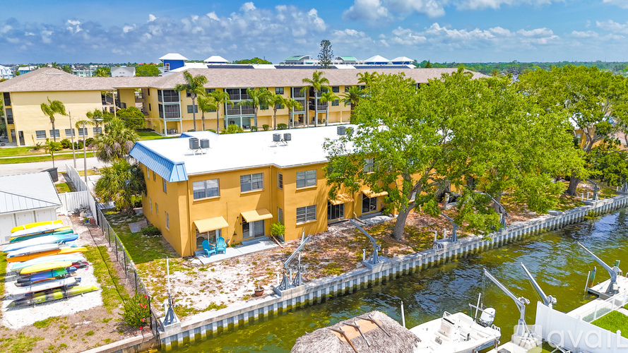 A yellow building with a blue roof is surrounded by trees and a body of water.