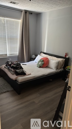 A bedroom with a neatly made bed and a window with blinds.