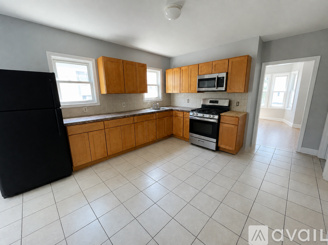 A kitchen with a black refrigerator, wooden cabinets, and white tiled flooring.