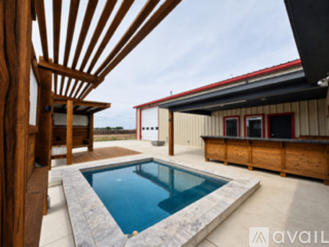 A wooden deck chair is in the foreground of a photo showing a pool and a building.