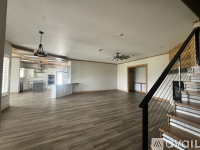 A spacious room with wooden floors and a staircase on the right side.