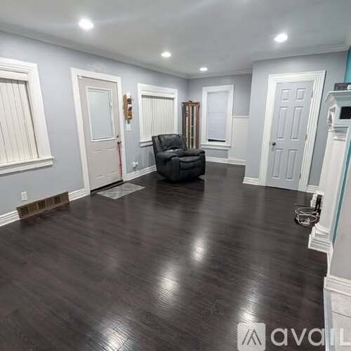 A spacious room with wood flooring and a black chair in the center.
