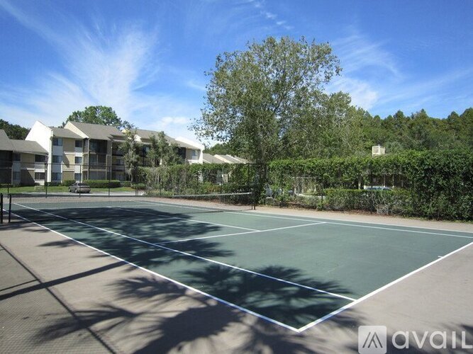 A tennis court is surrounded by trees and apartment buildings.