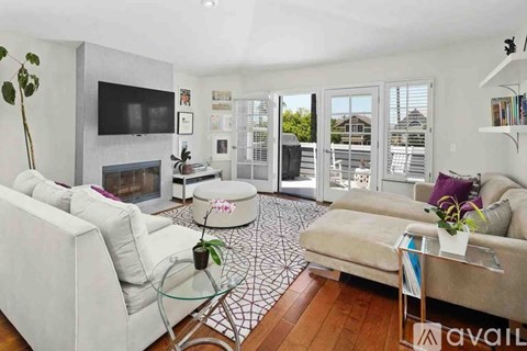 A living room with a white couch, a glass coffee table, and a television mounted on the wall.