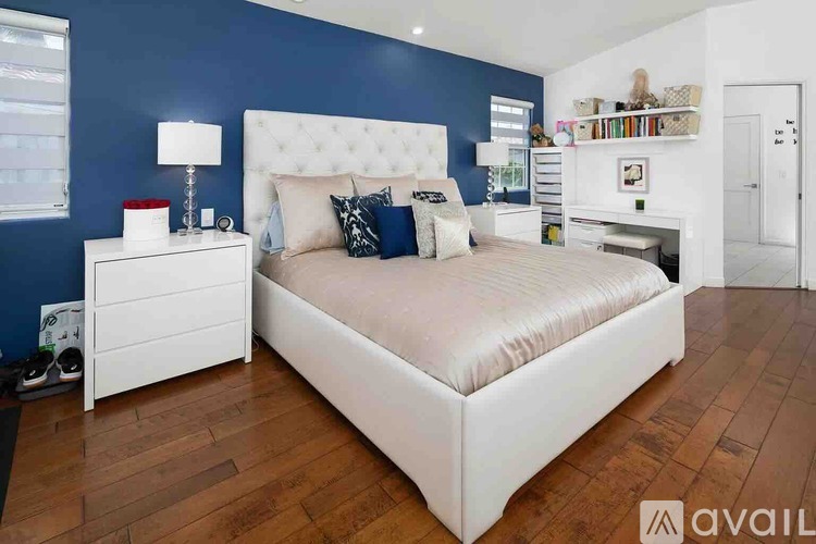 A bedroom with a white bed and a white nightstand with a lamp on it.