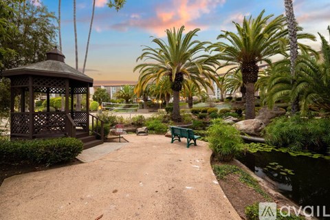 A gazebo is situated in a park with a bench and a pond.