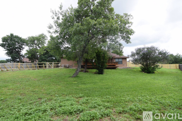 A grassy field with a tree and a house in the background.