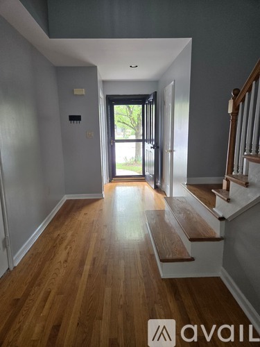 A hallway with wooden floors and a staircase on the right.