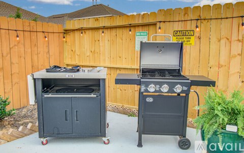 Two BBQ grills are on a patio with a caution sign in the background.