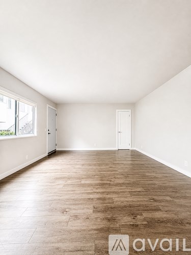 A room with wooden flooring and white walls, with a window on the left side.
